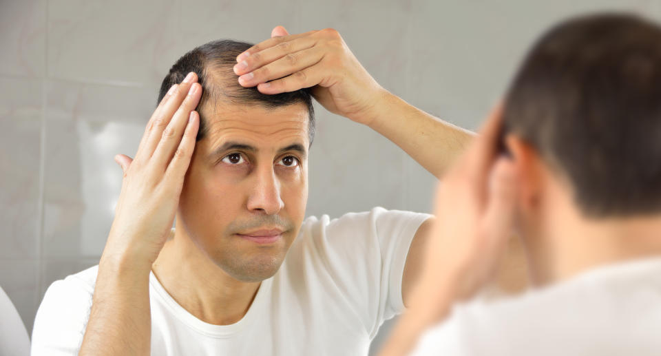 Man looking at hair in mirror. (Getty Images)