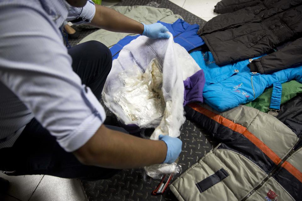 In this Jan. 26, 2014 photo, a police officer discovers bags of cocaine in the luggage of Liz Rabines, from Spain, at the anti-narcotics police station before she tried to embark a plane for Spain at the Jorge Chavez International Airport in Lima, Peru. While most of the mules are men, a growing number are women. (AP Photo/Martin Mejia)