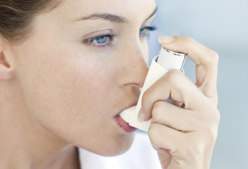 Woman with asthma using an inhaler for relief.