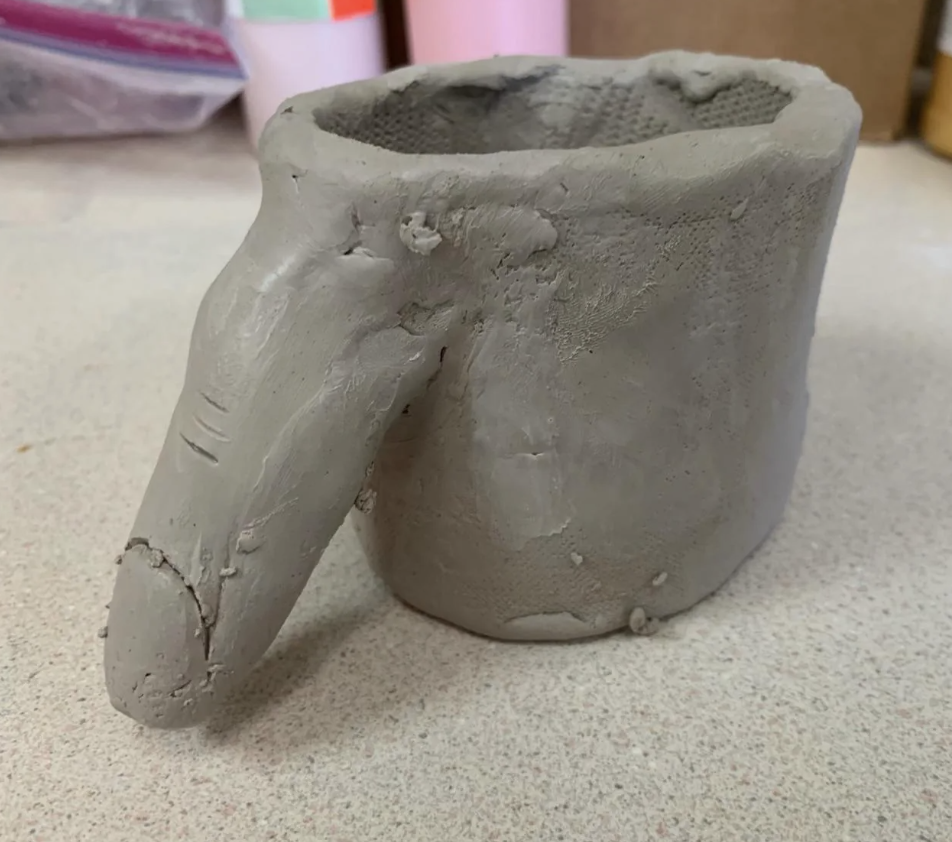 Clay mug with a unique, anthropomorphic handle resembling a finger. The image is categorized under Parents