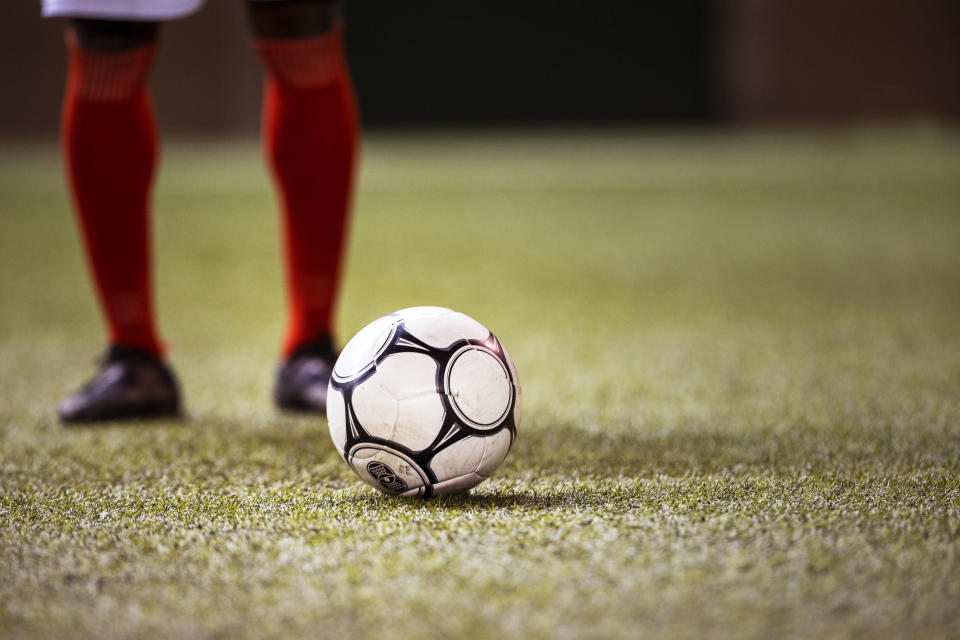 International football player wearing shin guards and cleats positions himself behind a soccer ball on a grass field in big athletic stadium and prepares to kick off professional championship game