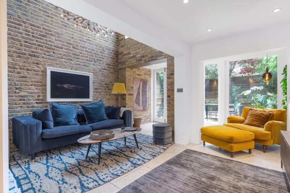 an image of the property's sitting area featuring a deep blue velvet 2 seater sofa and a mustard yellow chaise armchair along with two abstract rugs coffee table and stool