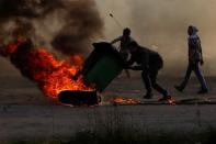 A Palestinian uses a trash container to move a burning tire during clashes with Israeli troops near the Jewish settlement of Beit El, near Ramallah, in the Israeli-occupied West Bank December 13, 2018. REUTERS/Mohamad Torokman