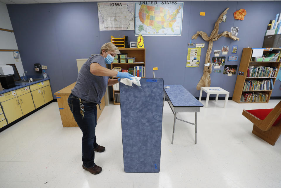 Des Moines Public Schools custodian Cynthia Adams cleans a desk in a classroom at Brubaker Elementary School, Wednesday, July 8, 2020, in Des Moines, Iowa. Getting children back to school safely could mean keeping high-risk spots like bars and gyms closed. That's the latest thinking from some public health experts. (AP Photo/Charlie Neibergall)