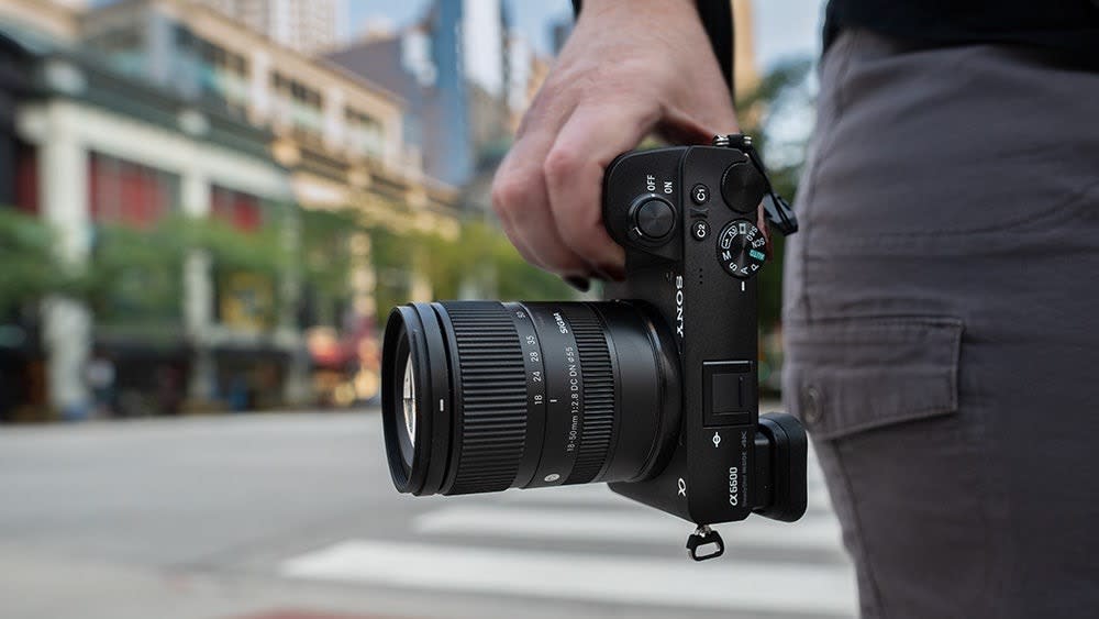  A hand holding a Sony camera with the Sigma 18-50mm f/2.8 DC DN lens attached. 
