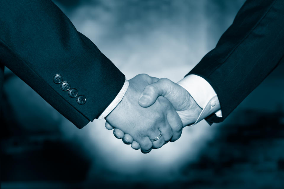 Two businessmen in suits shaking hands as if in agreement.