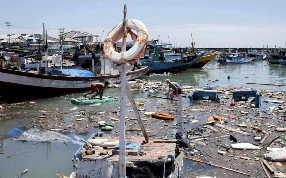 Indonesian men look for salvageable items amid debris and damaged boats following a storm at a port in Kupang, East Nusa Tenggara province, Indonesia Wednesday, April 7, 2021. Multiple disasters caused by severe weather in eastern Indonesia and neighboring East Timor have left a number of people dead or missing. (AP Photo/Armin Septiexan)