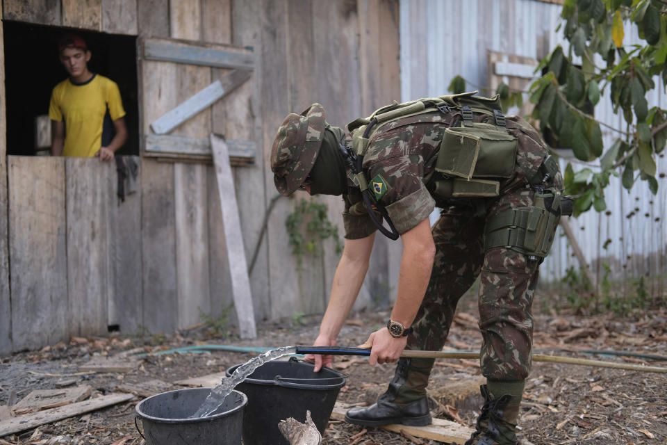 A member of Brazil's 17th brigade of jungle infantry fills up buckets with water at a property owned by the family of Eric Raauwendaal, left, at Jacunda National Forest, in the Amazonian state of Rondonia, Brazil, Thursday, August 29, 2019. A record number of fires in the Amazon has prompted an environmental crisis and a global outcry. (AP Photo/Luis Andres Henao)