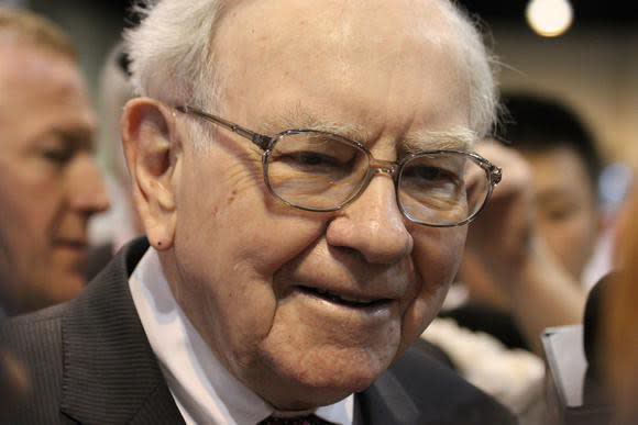 Warren Buffett smiling as he speaks with someone at a conference.