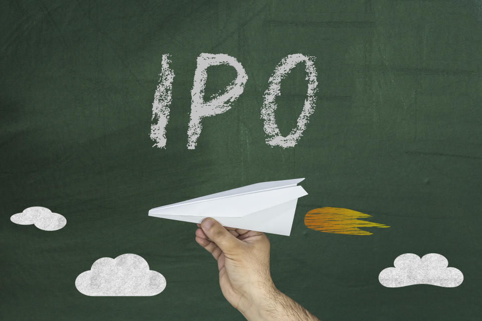 IPO written on a chalkboard with a hand holding a paper airplane with the appearance of flames drawn on the chalkboard behind the paper airplane over clouds.