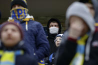 In this photo taken on Thursday, March 19, 2020, football fans of FC Bate, one of them wearing a face mask, watch the Belarus Championship soccer match between Energetik-BGU and Bate in Minsk, Belarus. Longtime Belarus President Alexander Lukashenko is proudly keeping soccer and hockey arenas open even though most sports around the world have shut down because of the coronavirus pandemic. The new coronavirus causes mild or moderate symptoms for most people, but for some, especially older adults and people with existing health problems, it can cause more severe illness or death. (AP Photo/Sergei Grits)