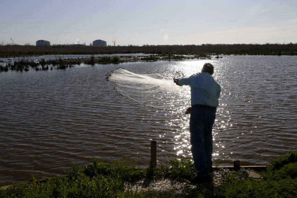 With the Venture Global LNG facility in the background, John Allaire throws a fishing net into a body of water on his property in Cameron, La., on Friday, April 1, 2022. Allaire, a retired environmental engineer in the oil and gas industry, is upset about emissions and noise and light pollution from a flare that has been burning frequently since the Venture Global site opened in recent months. He is fighting a second LNG export facility even closer to his property. "They would never do this (on) the coast of New Jersey or California or the East Coast or West Coast of Florida," he said of the LNG facilities that have proliferated along the Gulf Coast. (AP Photo/Martha Irvine)