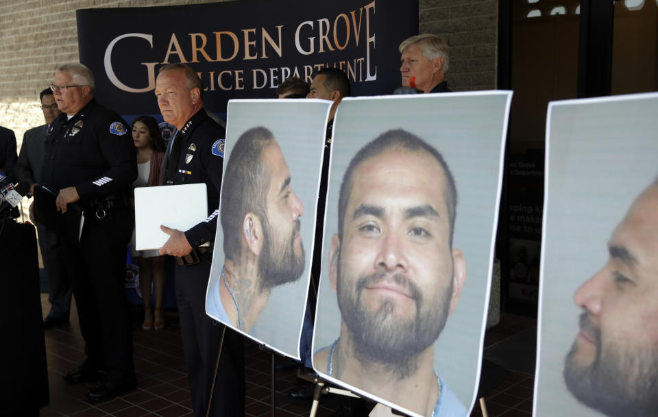 Garden Grove Police Chief Tom DaRe, center, and PIO Carl Whitney address the media next to a booking mug shot of Zachary Castaneda posted outside of the Garden Grove Police Department headquarters in Garden Grove, Calif., Thursday, Aug. 8, 2019. Investigators believe Castaneda, a documented gang member, stabbed several people to death and wounded a few others as he targeted his victims at random during a bloody rampage across two Southern California cities, authorities said. (AP Photo/Marcio Jose Sanchez)