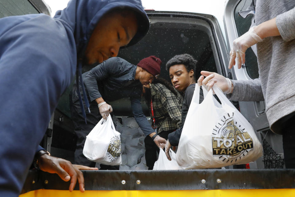 In this March 25, 2020, photo, volunteer JoJo Houston, 26, center, and Keshawn Jones, 16, right, help others to load a van with 150 bags of donated fresh produce as part of a Martha's Table initiative, along with community partners, to get food directly to the neighborhoods they serve, during a rainstorm in southeast Washington. The volunteers also loaded 50 more bags of groceries in a separate vehicle. These local volunteers are the tip of the spear for a grassroots community effort to keep Washington's most vulnerable neighborhoods fed during the unprecedented coronavirus crisis which has nearly shut down the American economy. (AP Photo/Jacquelyn Martin)