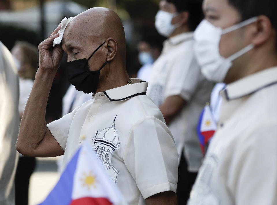 A masked city hall employee wipes sweat from his head during ceremonies in observance of National Flag Day outside Manila's city hall, Philippines on Thursday, May 28, 2020, as the capital observes community quarantine to avoid the spread of the new coronavirus. (AP Photo/Aaron Favila)