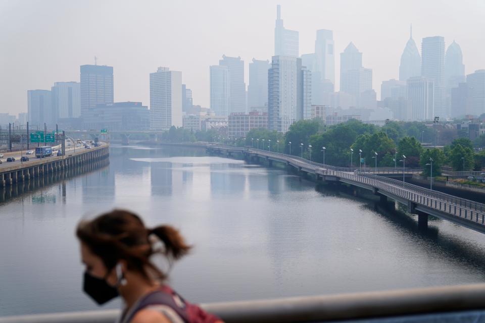A person wearing a protective face mask walks past the skyline in Philadelphia shrouded in haze, Thursday, June 8, 2023. Intense Canadian wildfires are blanketing the northeastern U.S. in a dystopian haze, turning the air acrid, the sky yellowish gray and prompting warnings for vulnerable populations to stay inside.