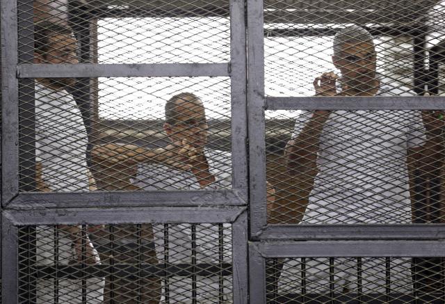 Al Jazeera journalists (L-R) Baher Mohamed, Peter Greste and Mohammed Fahmy stand behind bars in a court in Cairo in this June 1, 2014 file photo. Al Jazeera, the Qatari-funded television station whose reporting of the 2011 Arab Spring uprisings won it millions of viewers in the Middle East, is defiant following a backlash by Arab governments that accuse it of supporting Islamists. REUTERS/Asmaa Waguih/Files (EGYPT - Tags: POLITICS MEDIA CRIME LAW)