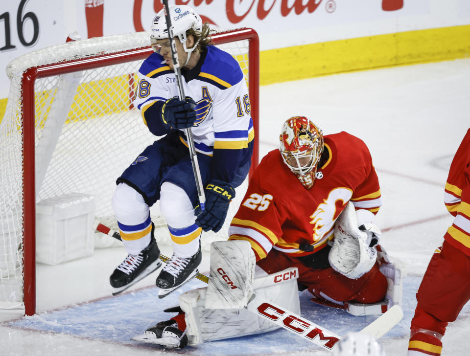 St. Louis Blues forward Robert Thomas, left, leaps out of the way of a teammate's shot on Calgary Flames goalie Jacob Markstrom during the second period of an NHL hockey game in Calgary, Alberta, Thursday, Oct. 26, 2023. (Jeff McIntosh/The Canadian Press via AP)