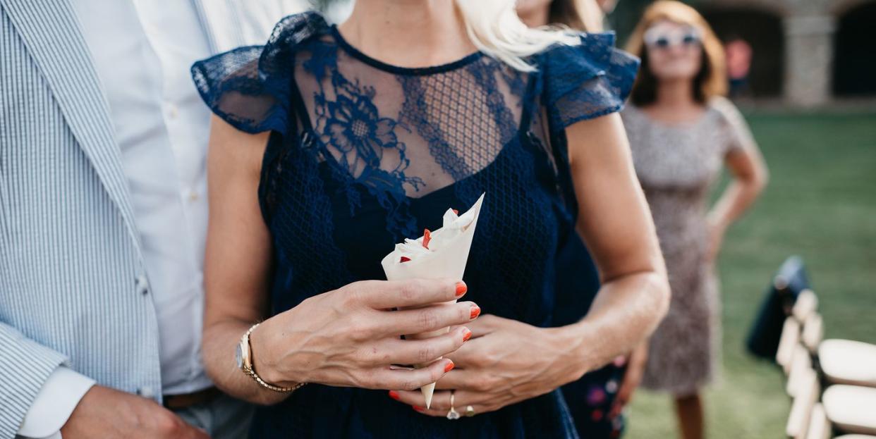 wedding guest in navy lace dress holding confetti