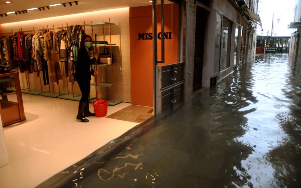 A woman mops up water in her flooded shop in Venice following Tuesday's high tide - AFP