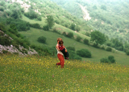 FILE PHOTO: An ethnic Albanian boy from Kosovo carries a refugee child into Albanian soil to escape fighting in Serbia's turbulent Kosovo province, June 7, 1998. The refugees walked more than 30 hours from their western Kosovo villages in the Decane area. REUTERS/Yannis Behrakis/File photo