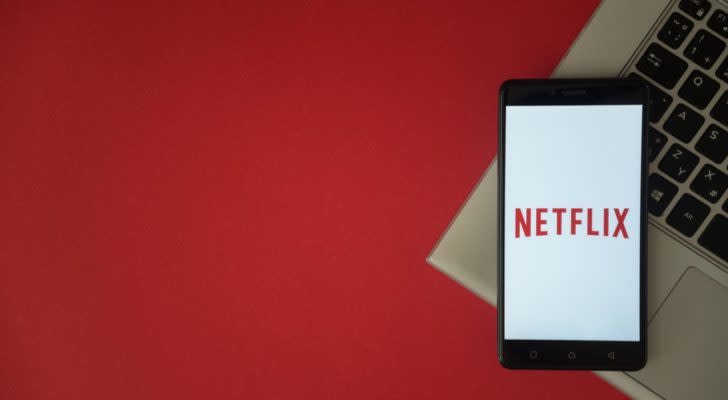 Netflix (NFLX) logo displayed on a phone which has a keyboard and red background behind it