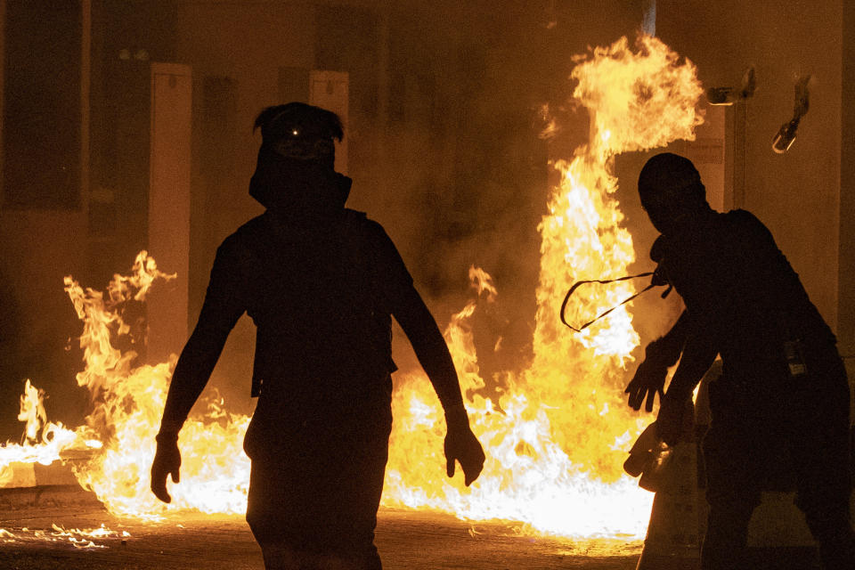 In this Thursday, Nov. 14, 2019, photo, protesters throw Molotov cocktails at the toll booth for the Cross Harbor Tunnel near the the Hong Kong Polytechnic University campus in Hong Kong in Hong Kong. Protesters who barricaded themselves inside Hong Kong’s universities have tried to turn the campuses into armed camps, resorting to medieval weapons to stop police from entering the grounds. Their weapons include bows and arrows, catapults and hundreds of gasoline bombs stacked up to ramparts - often built by the students. (AP Photo/Ng Han Guan)