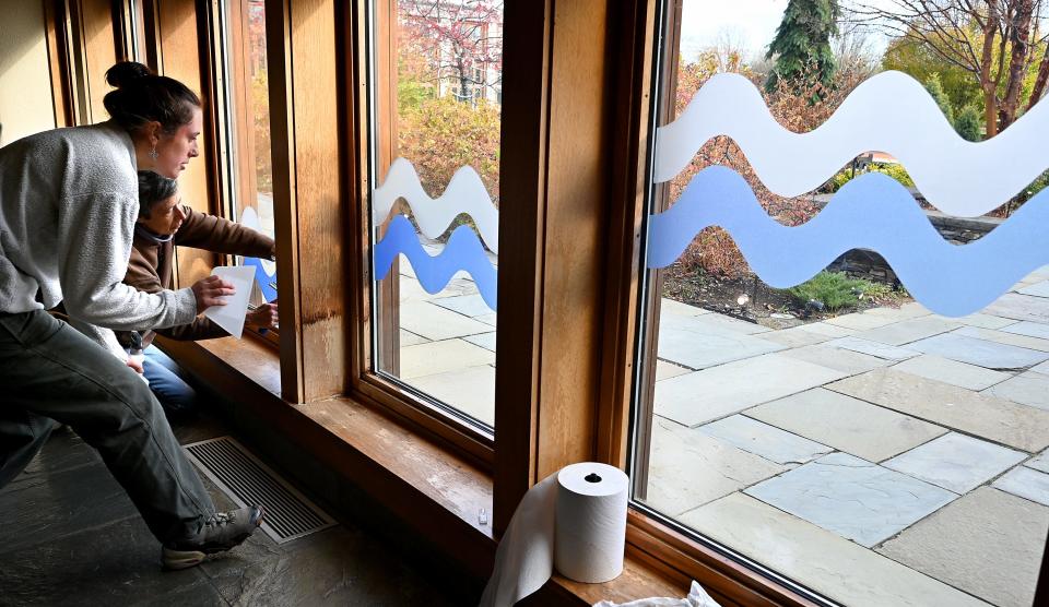Bella Bogdanski and Donna Doucette add waves representing an abstract movement of water to a hallway's windows. The New England Botanic Garden at Tower Hill in Boylston was setting up its 2022 Night Lights for the holidays.