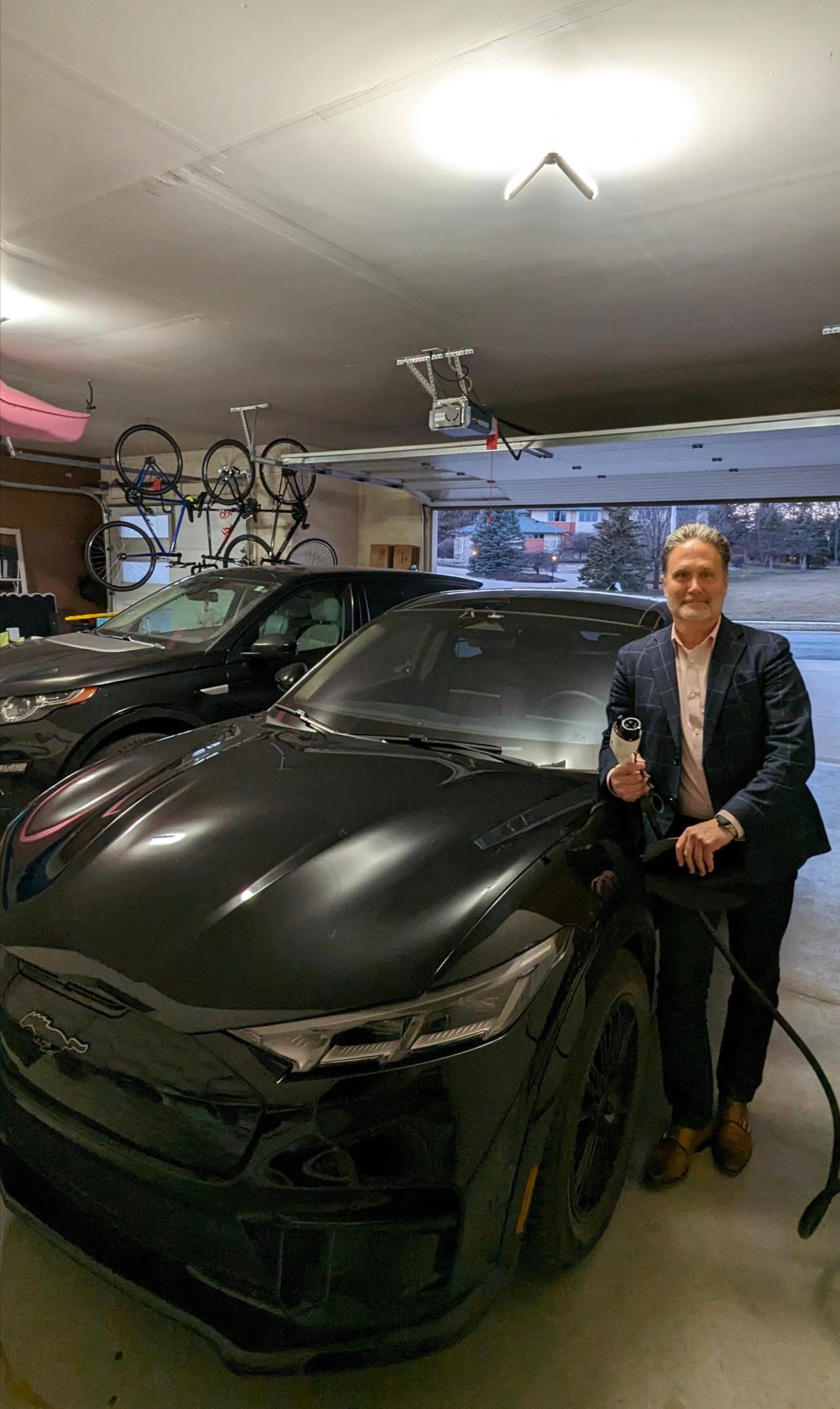 Zach Brandon of Madison, Wisconsin, stands beside his 2023 Ford Mustang Mach-E GT Performance Edition in his garage at home on Feb. 29, 2024. He has a home charging system and soon will receive a free charging adapter to access to the Tesla Superchargers network.
