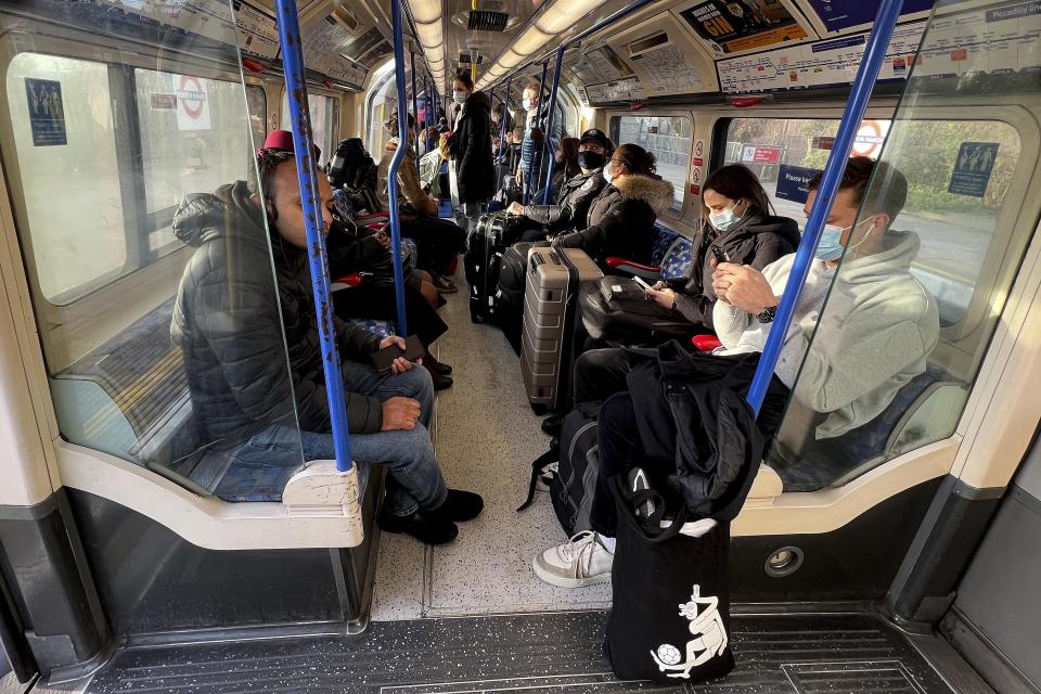 People mainly wearing face coverings sit on the Tube towards Heathrow Airport in London, Monday, Nov. 29, 2021. The new potentially more contagious omicron variant of the coronavirus popped up in more European countries on Saturday, just days after being identified in South Africa, leaving governments around the world scrambling to stop the spread. In Britain, Prime Minister Boris Johnson said mask-wearing in shops and on public transport will be required, starting Tuesday. (AP Photo/Frank Augstein)