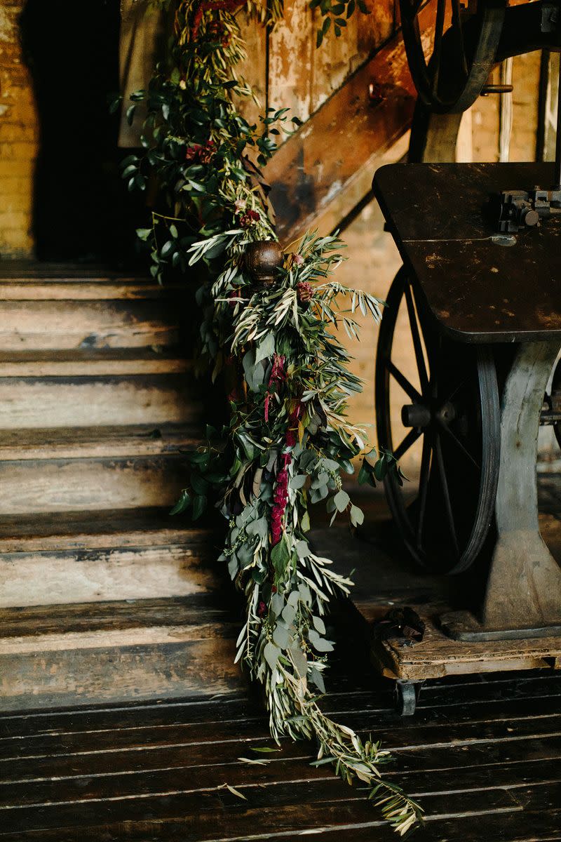 <p>Rather than cover every railing and table with floor to ceiling flowers, skip the blooms altogether and go green. Draped willow, eucalyptus, redwood, and spruce make for elegant decoration that feels inherently holiday, plus they'll leave behind a fresh scent. Garlands of greenery work on stairwells (as shown here), on fireplace mantles, or down each table at the reception, filled in as needed with moody objet and winter fruits and berries. </p><p><em>Pictured: Planning by <a href="http://www.jovemeyerevents.com/" rel="nofollow noopener" target="_blank" data-ylk="slk:Jove Meyer Events;elm:context_link;itc:0;sec:content-canvas" class="link ">Jove Meyer Events</a>.</em></p>