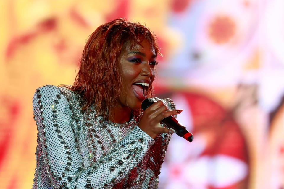 IZA performing on stage, wearing a sparkly, embellished top and holding a microphone