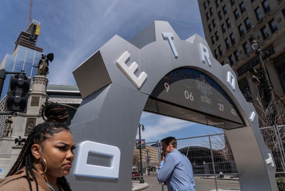 People walk past the countdown clock as work continues on the setup for the upcoming NFL Draft near Campus Martius in downtown Detroit on Tuesday, April 16, 2024.