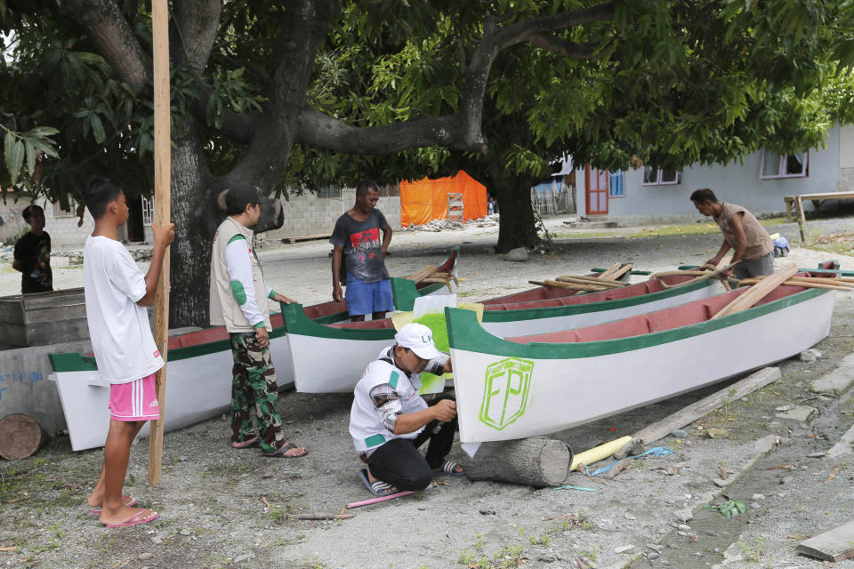 In this April 2, 2019, photo, members, center, of Islamic Defenders Front help local fishermen to build boats at a fishing village affected by the 2018 tsunami in Palu, Central Sulawesi, Indonesia. The Islamic Defenders Front, better known for vigilante actions against gays, Christmas decorations and prostitution, has over the past decade and a half repurposed its militia into a force that's as adept at searching for victims buried under earthquake rubble and distributing aid as it is at inspiring fear. In the process it has become an accepted and influential player in the world’s most populous Muslim-majority nation, and an accelerant in Indonesia’s decades old cultural war. (AP Photo/Tatan Syuflana)
