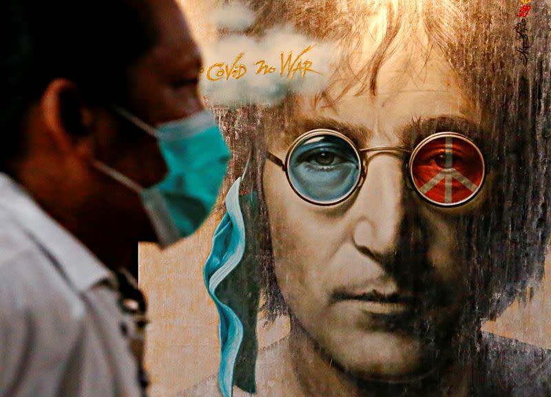 A visitor wearing a protective face mask walks past painted art depicting John Lennon during an exhibition, amid the coronavirus disease (COVID-19) outbreak, in Jakarta