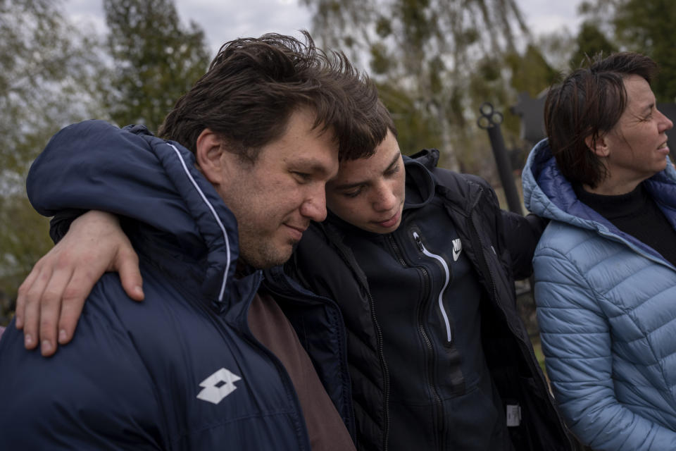 Yura Nechyporenko, 15, hugs his uncle Andriy Nechyporenko next to the grave of his father Ruslan Nechyporenko at the cemetery in Bucha, on the outskirts of Kyiv, Ukraine, on Monday, April 25, 2022. The teen survived an execution attempt by Russian soldiers while his father was killed, and now his family seeks justice. (AP Photo/Emilio Morenatti)