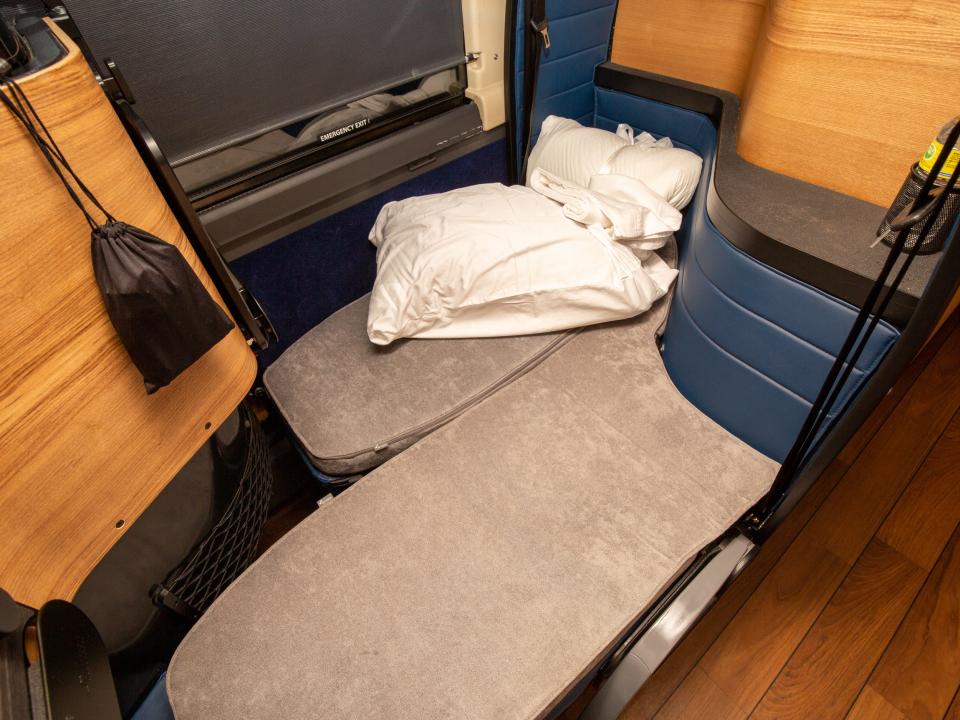 Two seats pulled down to reveal a grey bed topped with a pillow and a bundled mattress.