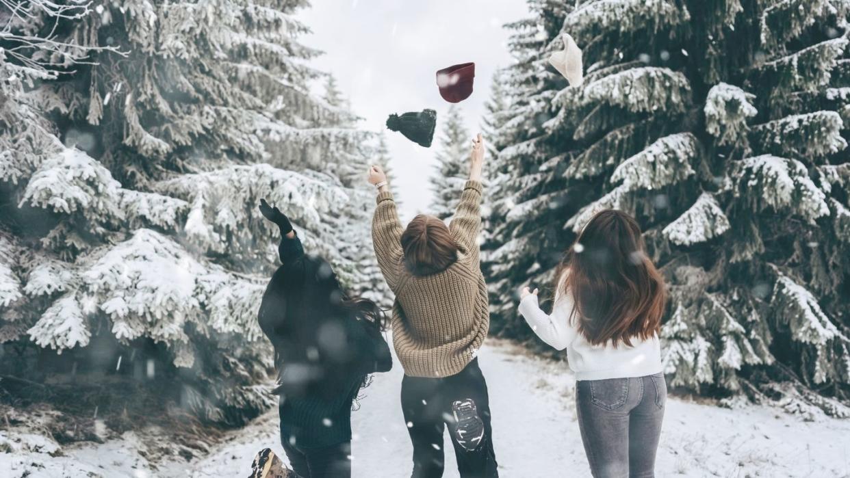 a group of three friends cheerfully jump and throw up their hats against the snow covered winter landscapewinter lifestyleenjoy the little things