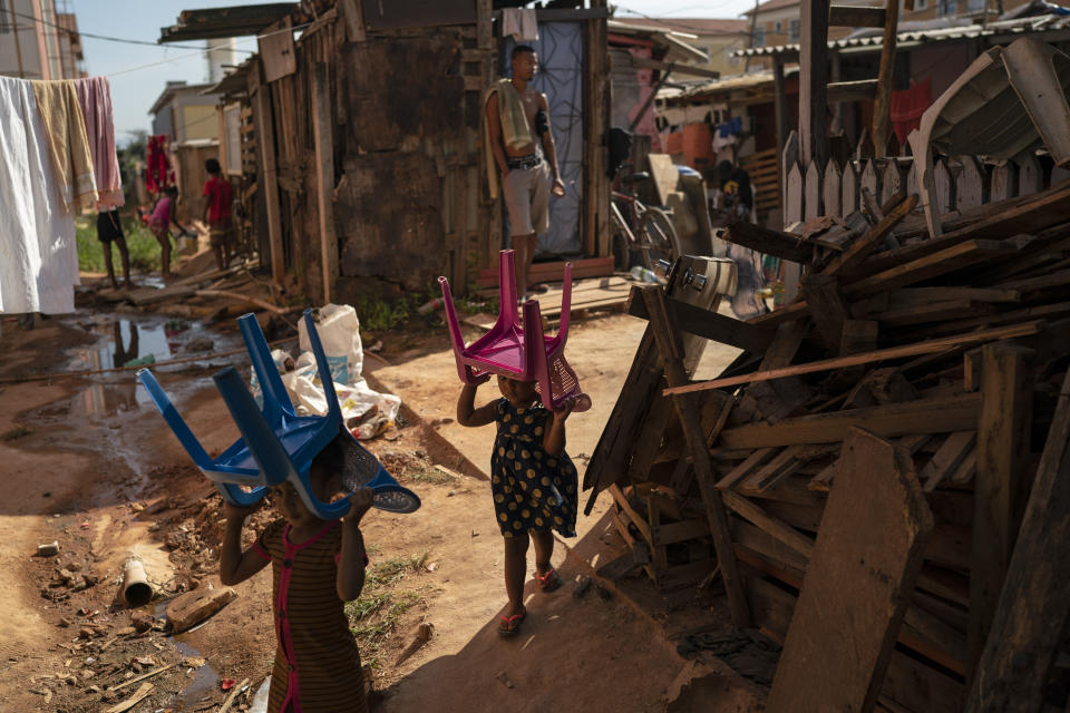 Children walk past carrying their chairs balanced on their heads, in an area occupied by squatters in a poor region amid the outbreak of the new coronavirus in Rio de Janeiro, Brazil, Friday, June 26, 2020. In this occupation, known in Portuguese as, "United We Will Win", about 200 families live in precarious conditions, with no proper sewage, where shacks are packed tightly together and the people have to share three communal bathrooms and a kitchen. (AP Photo/Leo Correa)