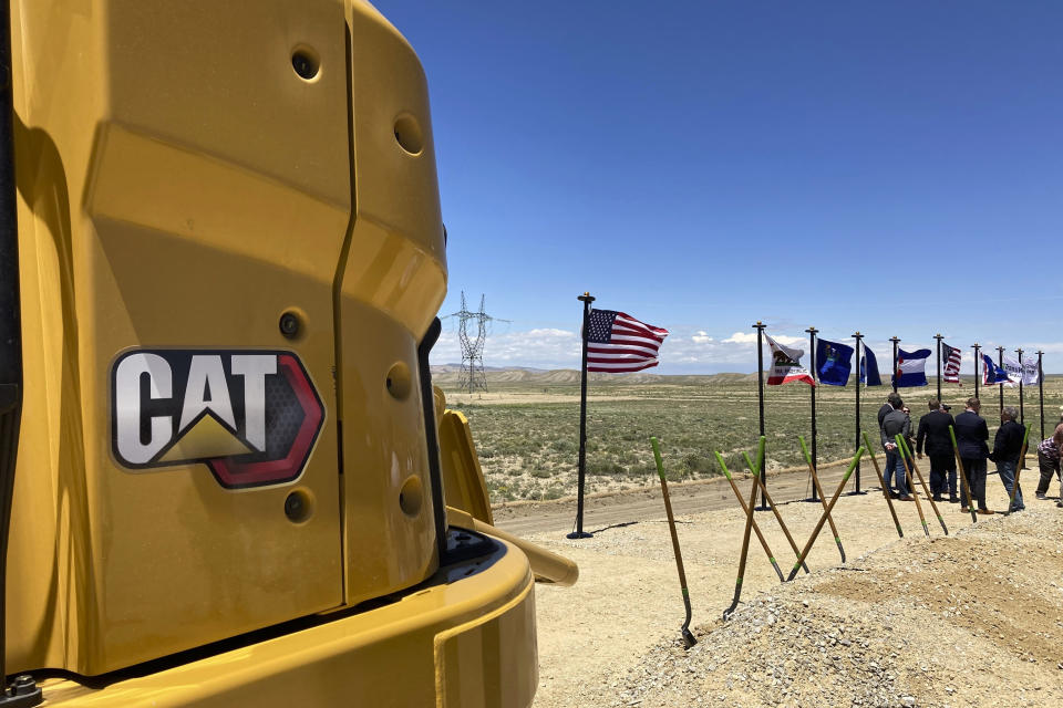 Heavy equipment sits at the site of a groundbreaking ceremony Tuesday, June 20, 2023, for the TransWest Express transmission line project south of Rawlins, Wyo., which will move electricity from a planned 600-turbine wind farm to California. The transmission line will partly parallel the PacifiCorp Gateway West transmission system visible in the distance. Wyoming is having a wind energy boom that could help alleviate climate change but is raising worries among residents that proliferating wind turbines will spoil views, disturb wildlife and kill birds. (AP Photo/Mead Gruver)