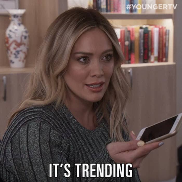 Hilary Duff in "Younger," holding a smartphone, looks concerned while saying, "IT'S TRENDING"