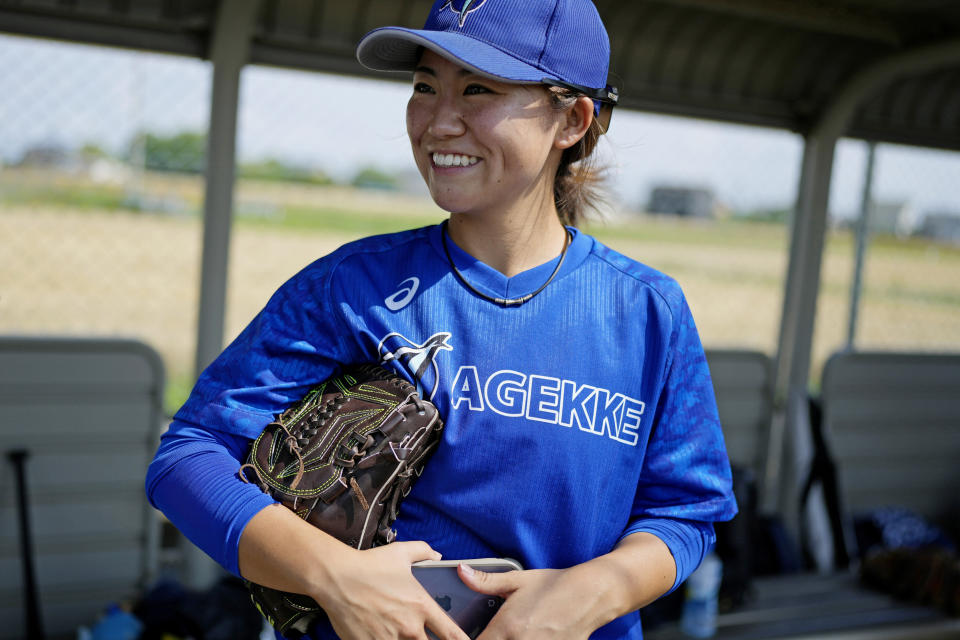 Eri Yoshida of a Japanese women's team, Agekke, smiles, with a backdrop of wheat field, during her team practice in Oyama, Tochigi prefecture, north of Tokyo, Tuesday, May 30, 2023. The 31-year-old Japanese woman is a knuckleball pitcher with a sidearm delivery that she hopes might carry her to the big leagues in the United States or Japan. (AP Photo/Shuji Kajiyama)