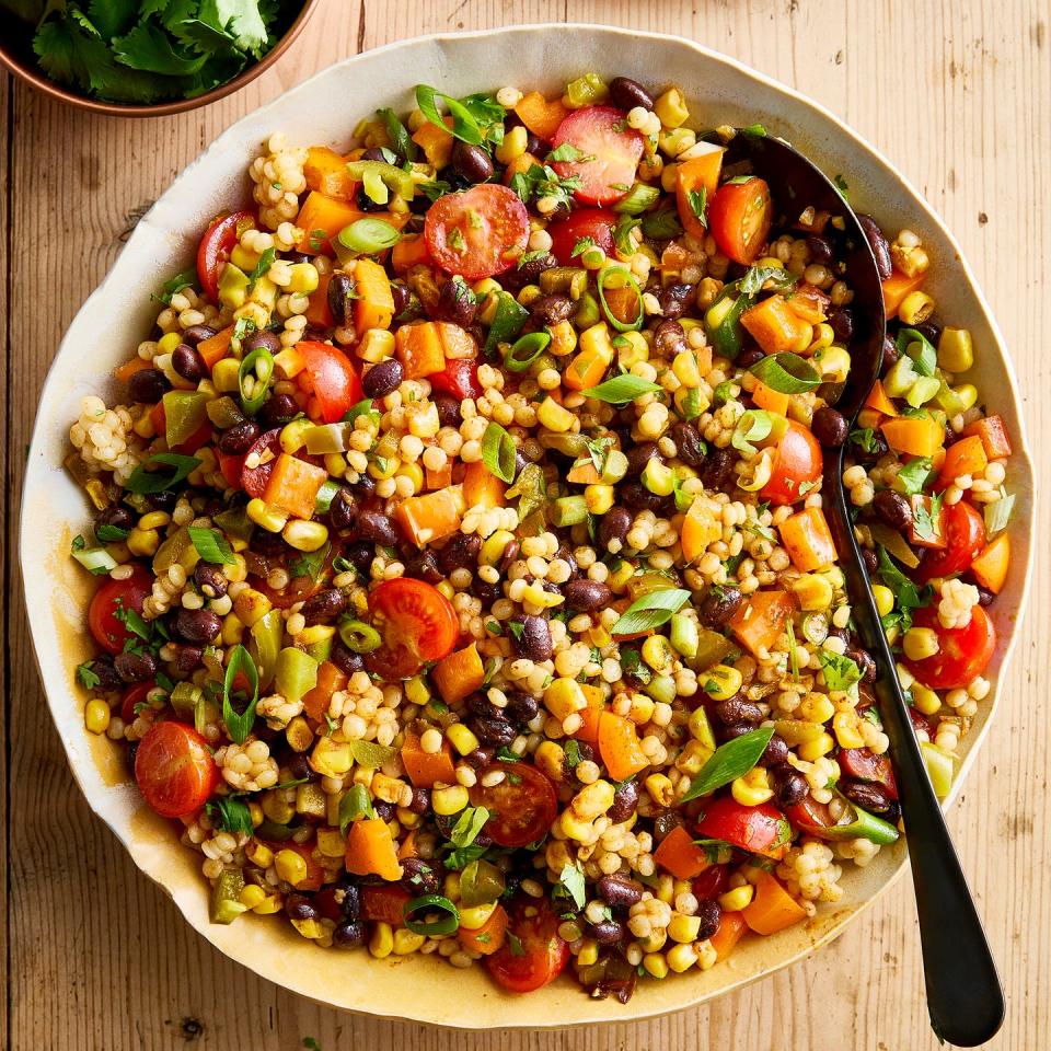 a bowl with pearl couscous, black beans, corn, bell peppers, cherry tomatoes, scallions, cilantro, and pickled jalapenos