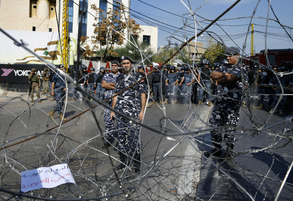 Lebanese troops and riot police, stand guard behind barbed wire, as a few dozen people demonstrate and chant slogans, during a protest against what they called, "America's intervention in Lebanon's affairs," near the U.S. embassy in Aukar, northeast of Beirut, Lebanon, Sunday, Nov. 24, 2019. Arabic at lower left corner reads, "police state protects Zionists." (AP Photo/Bilal Hussein)