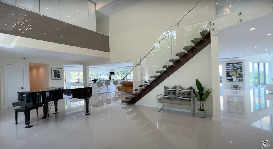 The foyer of a house with a piano and a floating staricase.