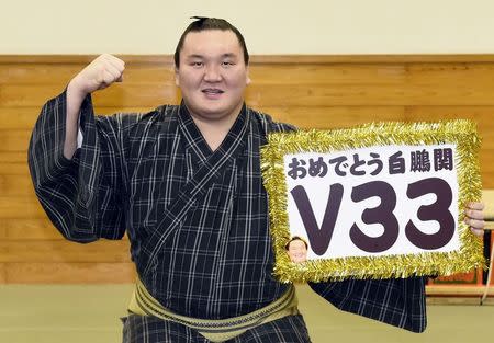 Mongolian-born grand sumo champion Yokozuna Hakuho poses for photos with a board reading "Congrats Hakuho V33" after winning the New Year Grand Sumo Tournament in Tokyo January 23, 2015, in this photo taken by Kyodo. Mandatory Credit REUTERS/Kyodo