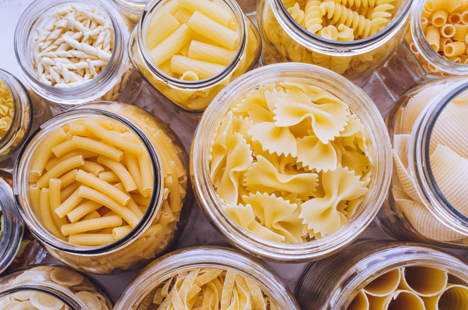 Variety of types and shapes of Italian pasta in glass jars on marble background. Italian cuisine food storage concept. Top view. Copy space.