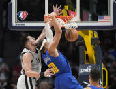 Denver Nuggets forward Aaron Gordon, right, hangs from the rim after a dunk next to San Antonio Spurs forward Drew Eubanks during the first half of an NBA basketball game Friday, Oct. 22, 2021, in Denver. (AP Photo/David Zalubowski)