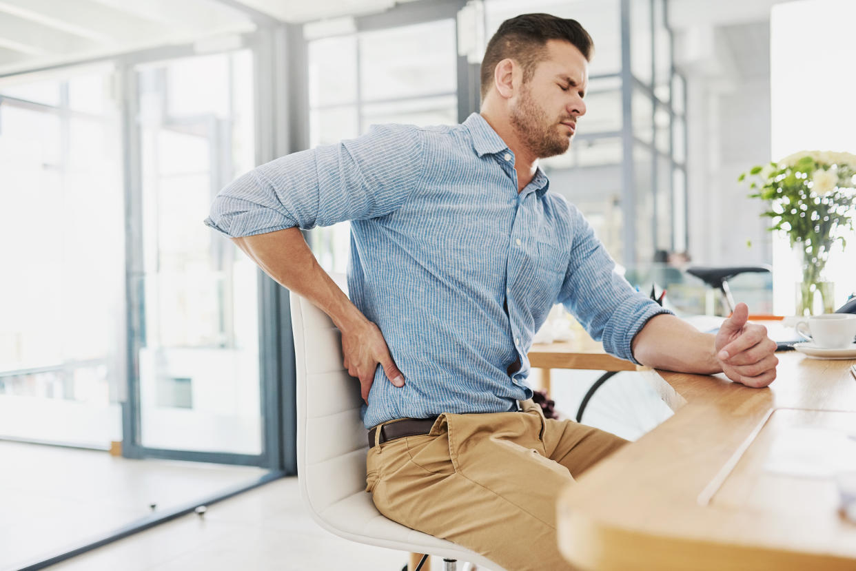 Cropped shot of a young businessman experiencing back pain while working at his desk