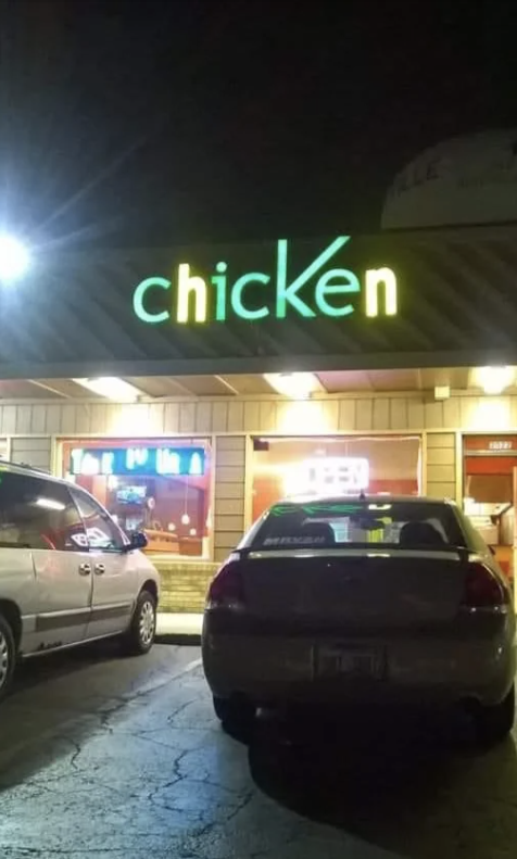 Sign reading 'chicken' above a lit storefront at night with parked cars in the foreground